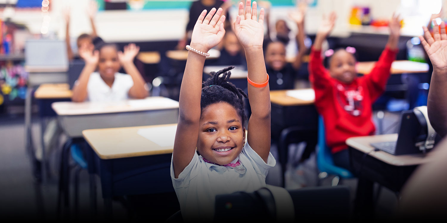 Smiling students raising hands in a classroom.
