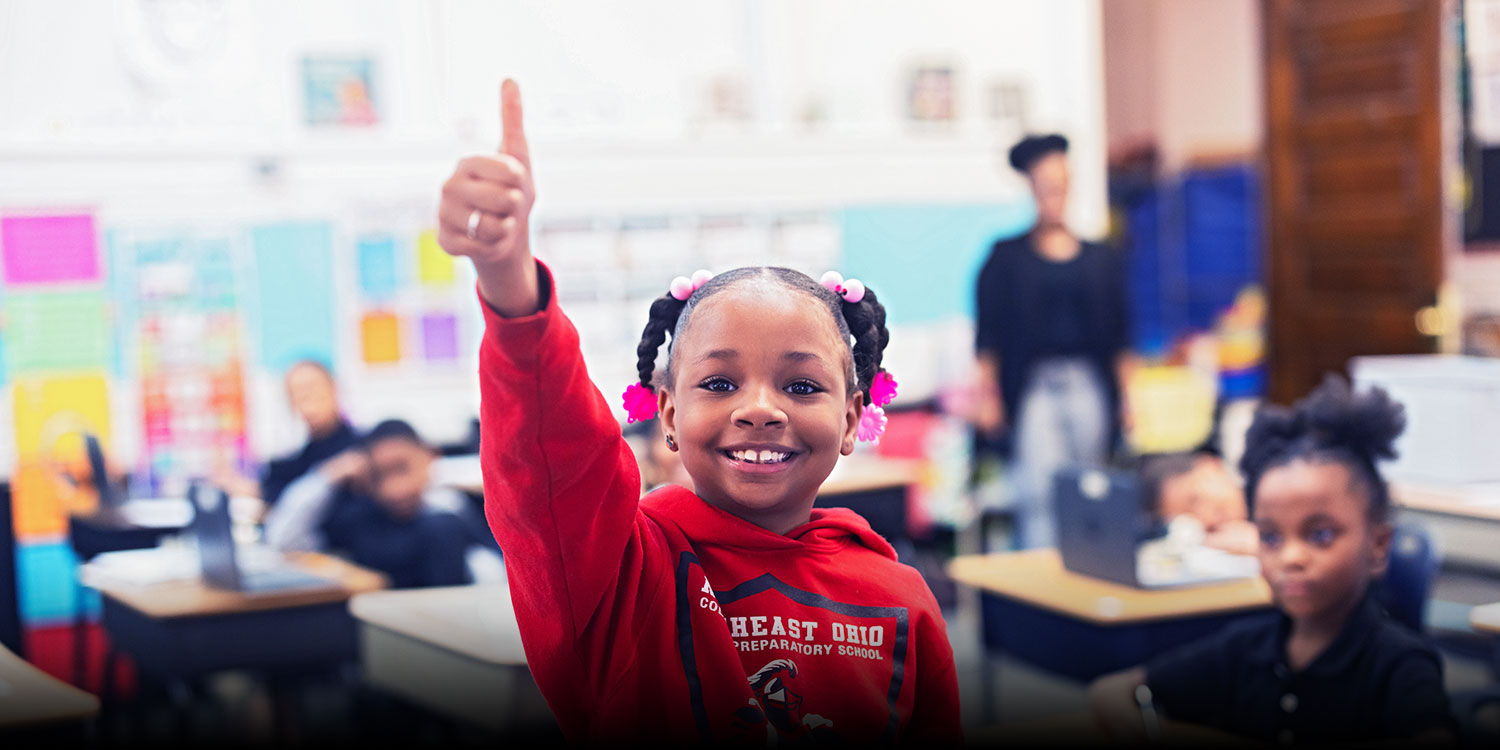 Smiling student giving thumbs up in a classroom.